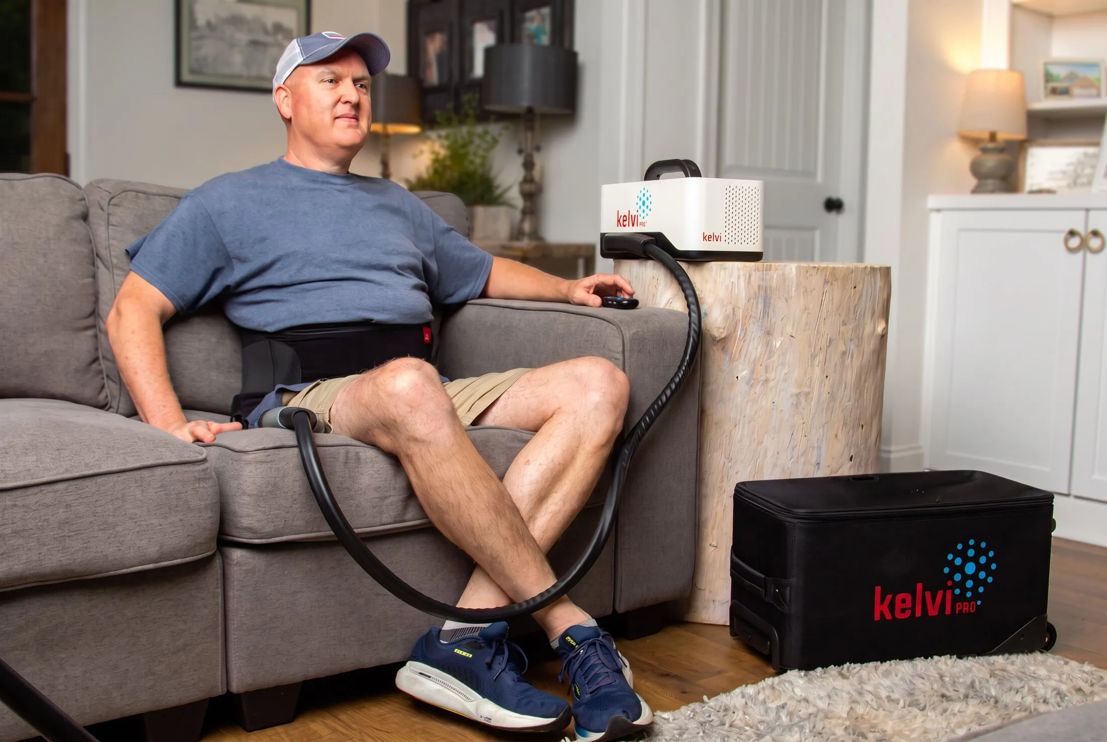 A man using a Kelvi back wrap at home, with the Pro console and travel case beside him