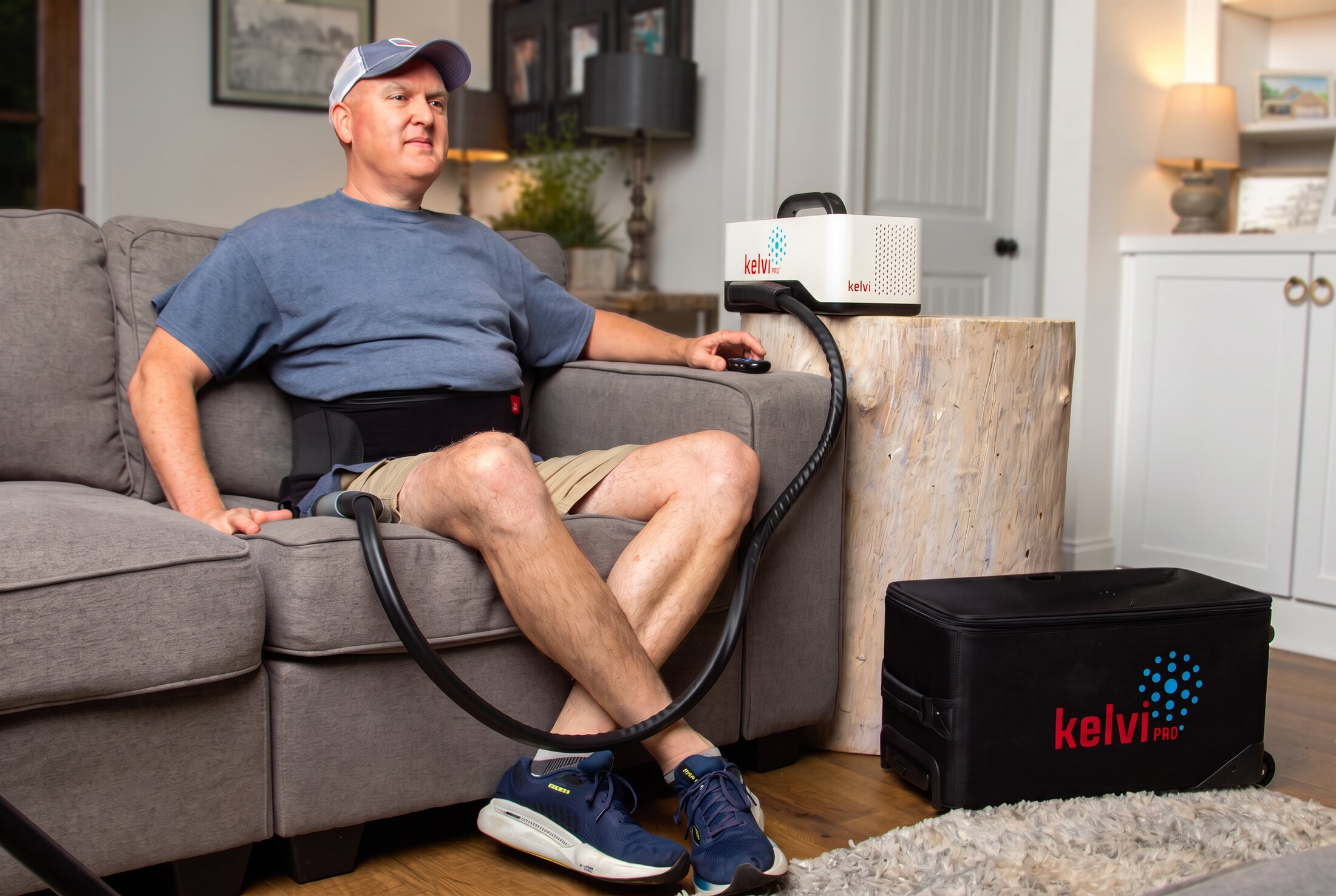 A man using a Kelvi back wrap at home, with the Pro console and travel case beside him